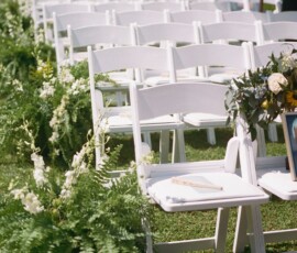 White folding chairs with greenery and flowers line a grassy aisle for a New Orleans wedding; bouquet and photo on front row chair.