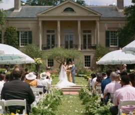 Outdoor wedding ceremony on a sunny day with white chairs, green aisle decor, and a mansion backdrop—ideal Louisiana inspiration.