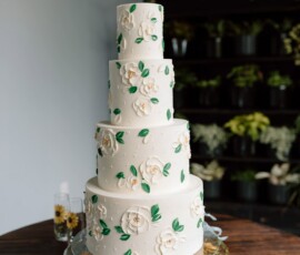 Elegant four-tier white cake with flowers and greenery on a glass stand, ideal for a romantic Louisiana wedding.