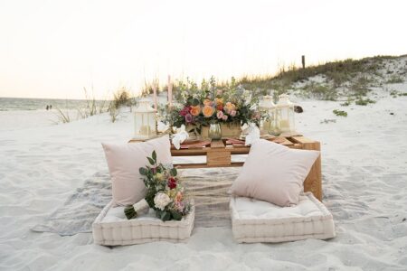 Beach picnic table with floral arrangements, candles, and cushioned seats—ideal for a romantic New Orleans wedding.
