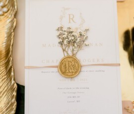 Wedding invitation with gold wax seal, babys breath, white rose, gold tray, and blush ribbon in soft gold and blush tones.