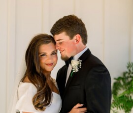Bride in white dress and veil embraces groom in black suit, both smiling softly—romantic Louisiana wedding moment.