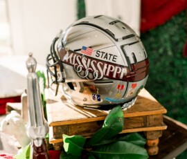 Mississippi State football helmet on books with greenery, red cloth, and decor—unique New Orleans wedding inspiration.