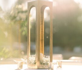 Gold lantern with white candle on a wedding table in Louisiana, surrounded by white flowers, votives, and sunlight.