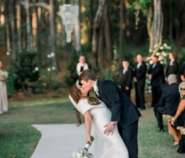 Bride and groom kiss at the end of an outdoor aisle, surrounded by trees and guests at a Louisiana wedding.