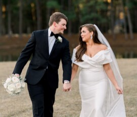 Bride in white gown and groom in black suit smile at each other, holding hands outdoors at their Louisiana wedding.
