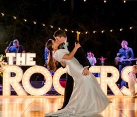 Bride and groom kiss during their first dance at night with live band and THE ROCKERS lights in the background.