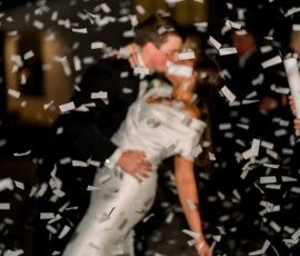 A couple in formal wear kisses while dancing amid confetti, celebrating a joyful Louisiana or Gulf South wedding.
