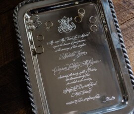 Ornate silver tray with rings and engraved wedding invitation on rustic wood, evoking New Orleans wedding charm.