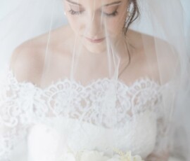 Bride in lace wedding dress with white and blush bouquet, gazing down under a sheer veil—romantic New Orleans inspiration.