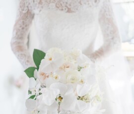 Bride in off-the-shoulder lace dress holds white orchids and roses bouquet, indoors at a Louisiana wedding ceremony.