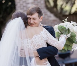 Bride in lace dress and groom embrace outdoors at their Louisiana wedding, sharing a joyful moment and white bouquet.