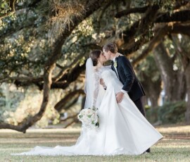 Bride and groom share a kiss under large trees at their New Orleans wedding, sunlight filtering through the branches.
