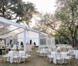 Louisiana outdoor wedding with round tables, gold chairs, white linens, floral centerpieces, string lights, and festive trees.