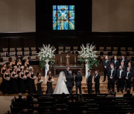 Bride and groom at a New Orleans church altar, with bridal party in black and stained glass above for classic wedding inspiration.