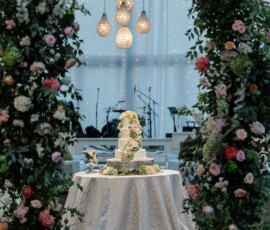 Elegant tiered wedding cake with pink flowers, floral arches, and string lights at a classic Louisiana wedding reception.