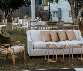 Chic outdoor lounge with white sofa, gold accents, bamboo chair, and candles—ideal wedding inspiration on a grassy lawn.