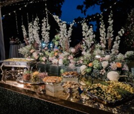 Chic outdoor buffet table with white flowers, greenery, and appetizers under string lights at a New Orleans wedding reception.
