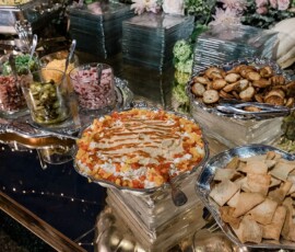Buffet table with pita chips, bread, dips, pickles, meats, and cheese in silver dishes at a Louisiana wedding reception.