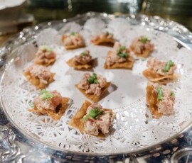 Silver tray with doily holds crackers topped with pink spread and green herbs—ideal for elegant New Orleans weddings.