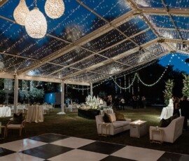Nighttime outdoor event under a clear tent with string lights, white sofas, checkered dance floor, and New Orleans wedding charm.