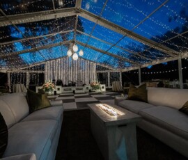 Outdoor Louisiana wedding at night under a clear tent with string lights, chandeliers, white couches, and checkered dance floor.