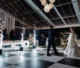 Bride and groom dance on a checkered floor under string lights, with guests and pyrotechnics at their Louisiana wedding reception.