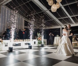 Bride and groom share their first dance on a checkered floor under string lights, sparklers, and admiring guests in Louisiana.