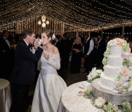 Bride and groom toast with champagne under string lights at a New Orleans wedding, guests and floral cake nearby.