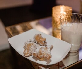 Powdered sugar pastries on a white plate with milk and a lit candle, perfect for Louisiana wedding inspiration.