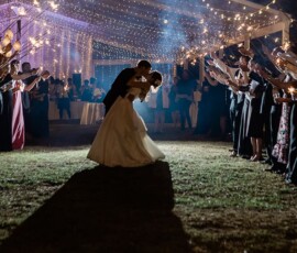 A couple kisses under a tunnel of guest-held sparklers at their outdoor Gulf South wedding reception at night.