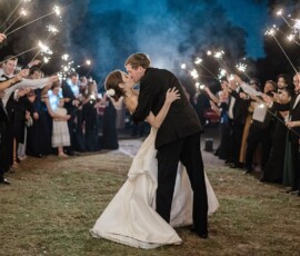 Bride and groom kiss under a sparkling archway of guests at a magical outdoor Louisiana wedding.
