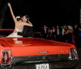 Bride and groom embrace in a red convertible at night, bride waving as guests stand under string lights at a New Orleans wedding.