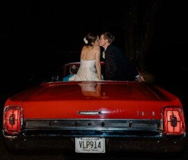 Bride and groom kiss on a red vintage car at night, dressed for a classic Louisiana wedding.