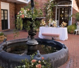 Black tiered fountain with peach and white flowers in a brick courtyard, set for a romantic Louisiana wedding.