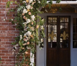 Brick building entrance with wooden doors, adorned with white and peach roses, greenery, and branches for a Gulf South wedding.