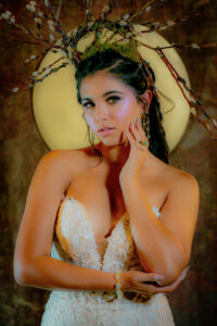 Woman in a white textured dress poses with a branch headpiece before a glowing circular backdrop.