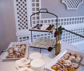 Dessert table with powdered pastries, cookies, plates, napkins, and a gold rose vase in an elegant white lattice room.