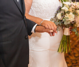 Bride in white dress with bouquet links arms and holds hands with person in dark suit as they walk on their wedding day.
