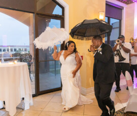 Bride and groom dance joyfully with decorative umbrellas as a lively brass band plays during their grand entrance.