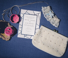 Wedding accessories on blue: lace garter, pearl purse, silver necklace, bangles, ring boxes, tray, geometric invitation.