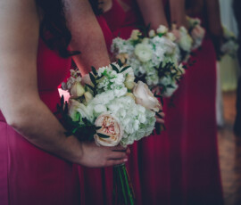 Bridesmaids in pink dresses stand in a row, holding white and light pink bouquets at a wedding ceremony.