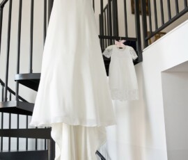 A white wedding dress and lace dress hang on a black spiral staircase in a bright room, inspiring New Orleans weddings.