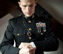 Man in formal military uniform adjusts sleeve indoors with wooden beams, evoking classic Louisiana wedding inspiration.