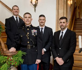 Four men in formal attire stand by a greenery-adorned staircase at a classic Louisiana wedding, candles adding elegance.