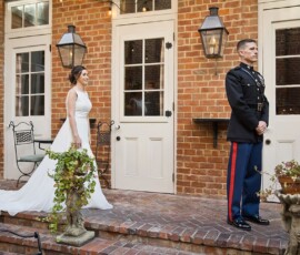 Bride in white gown stands behind groom in military uniform on brick patio for a first look at Gulf South wedding.