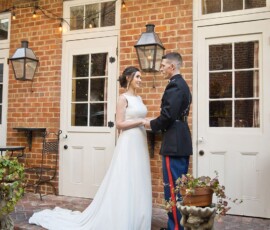 Bride in white gown and groom in military uniform hold hands on brick steps under string lights—Gulf South wedding inspiration.