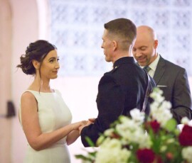 Bride and groom hold hands at their Louisiana wedding, smiling officiant behind them, floral arrangements in front.