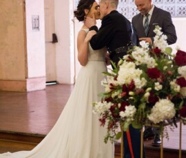 Bride and groom kiss at their New Orleans wedding ceremony, with officiant and floral arrangement in view.