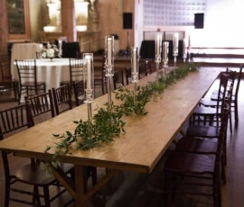 Elegant New Orleans wedding table with dark chairs, greenery, glass candle holders in a spacious, softly lit room.